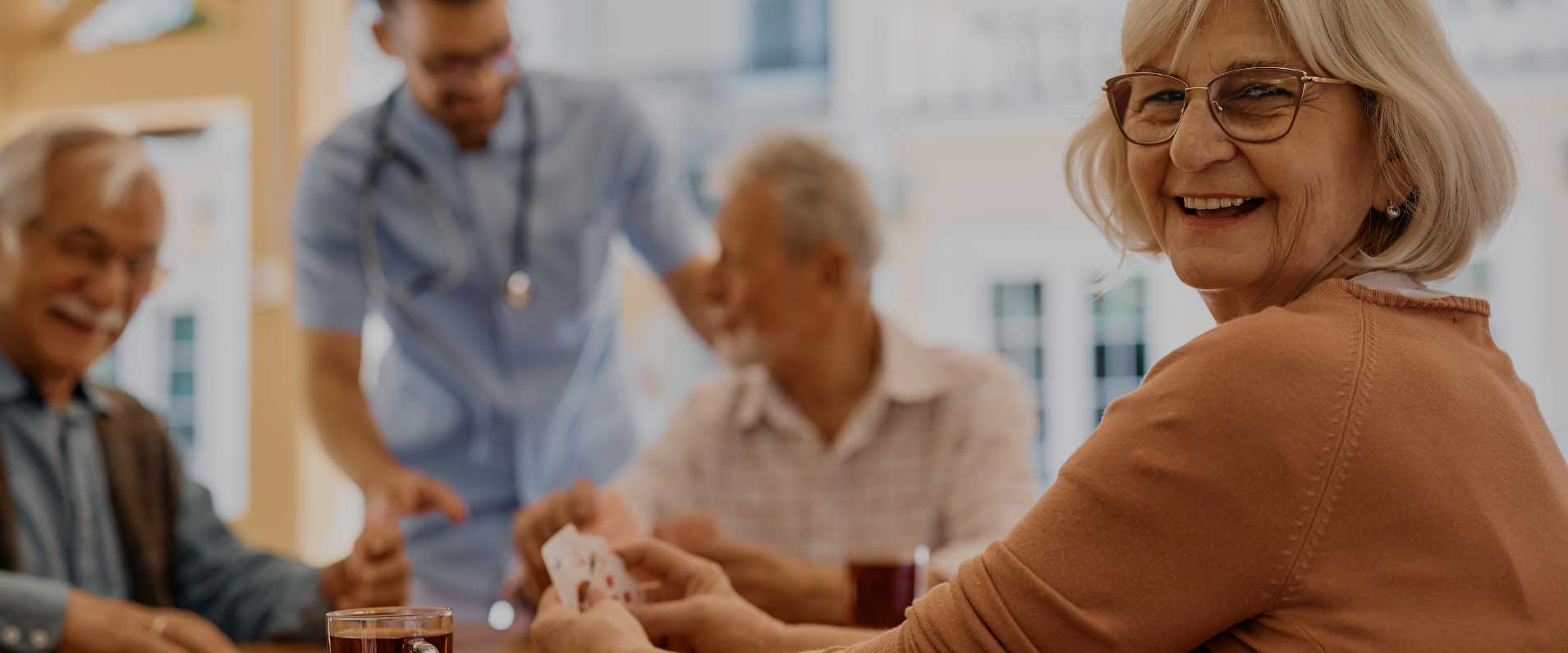 Smiling senior residents playing cards with a caregiver
