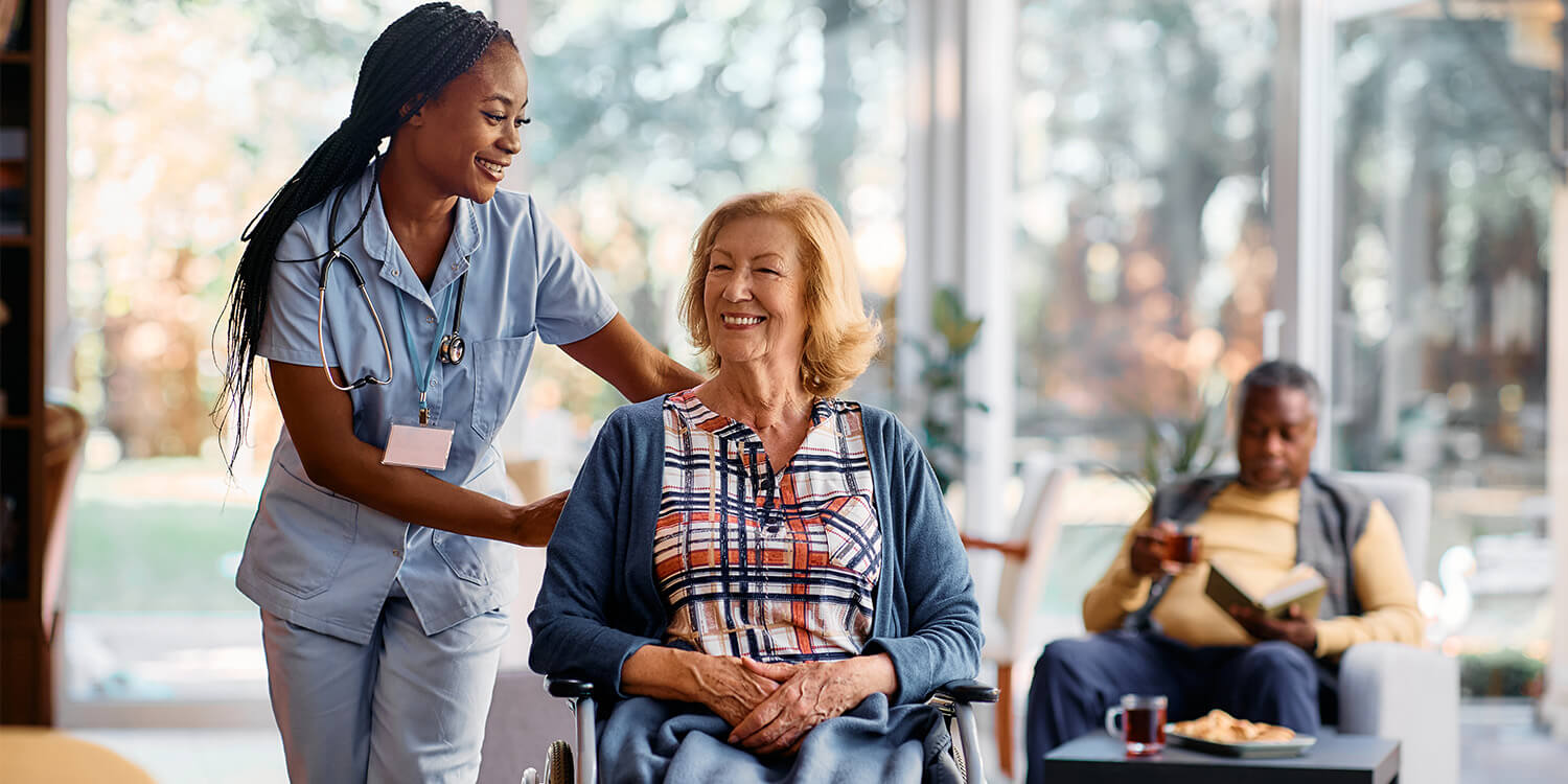 Caregiver greeting smiling senior residents in a bright assisted living sunroom