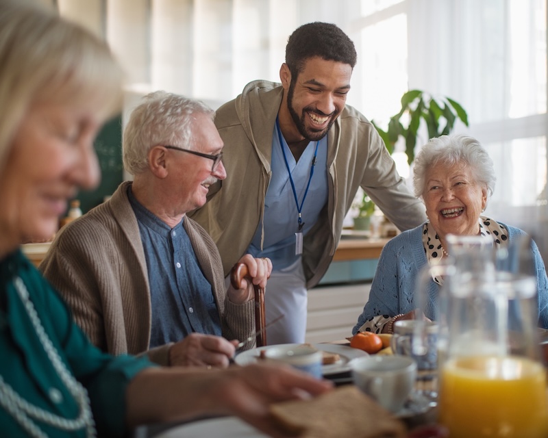 Group of cheerful seniors enjoying breakfast with a staff member at a nursing home