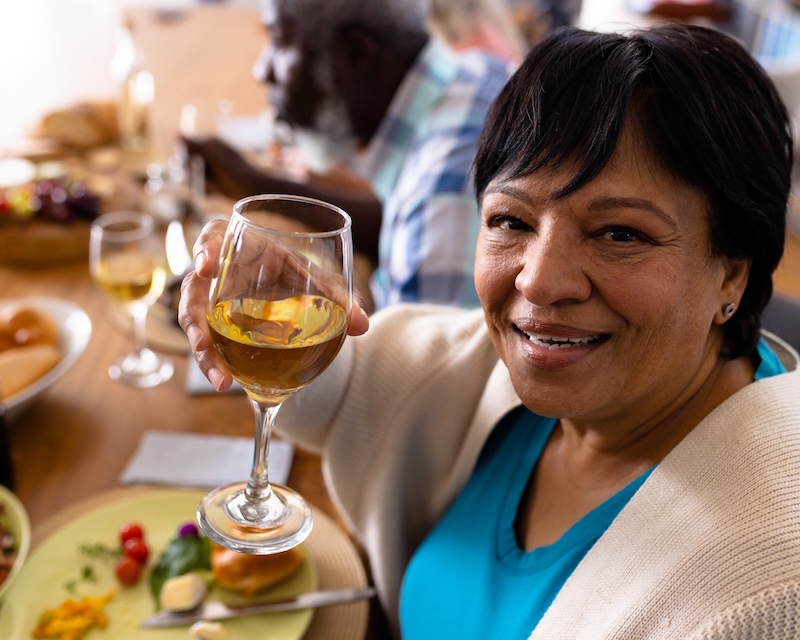 Smiling senior woman raising a glass of white wine at dinner