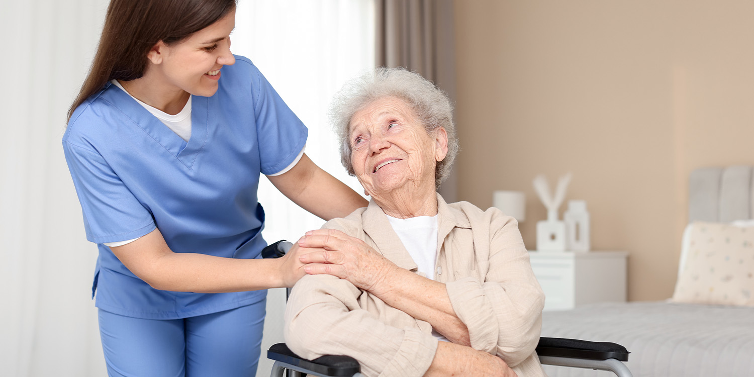 Nurse in blue scrubs comforting a smiling senior woman in a wheelchair