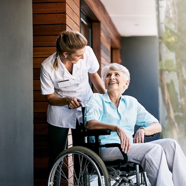 Caregiver pushing a smiling senior woman in a wheelchair