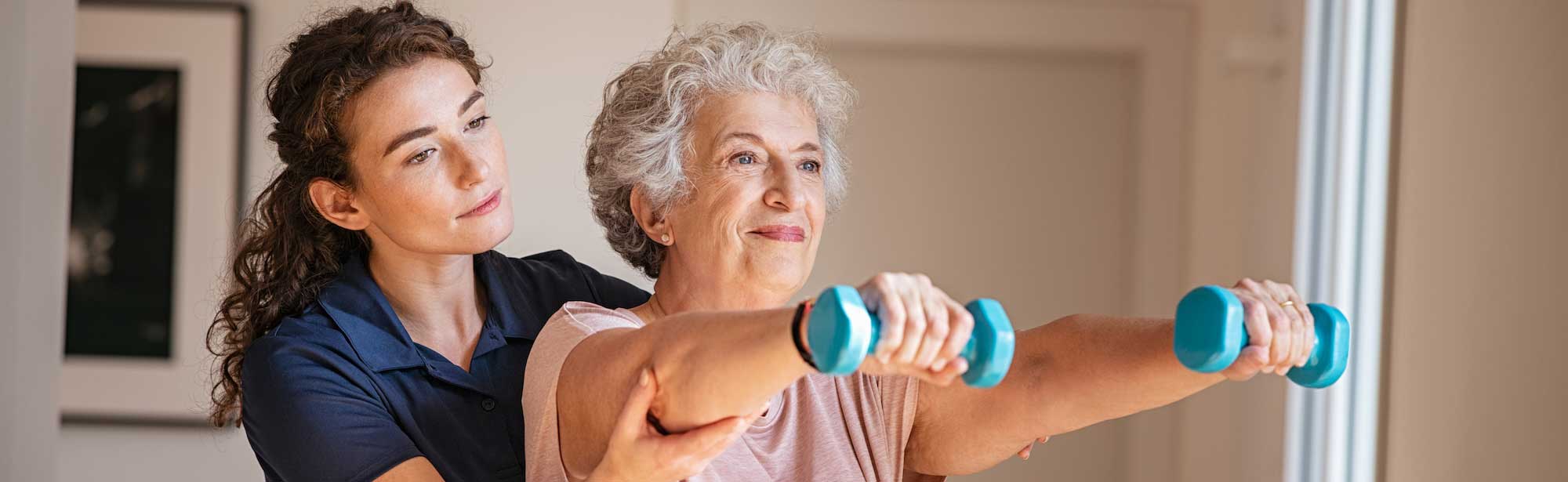 Therapist guiding a senior woman through a dumbbell arm exercise